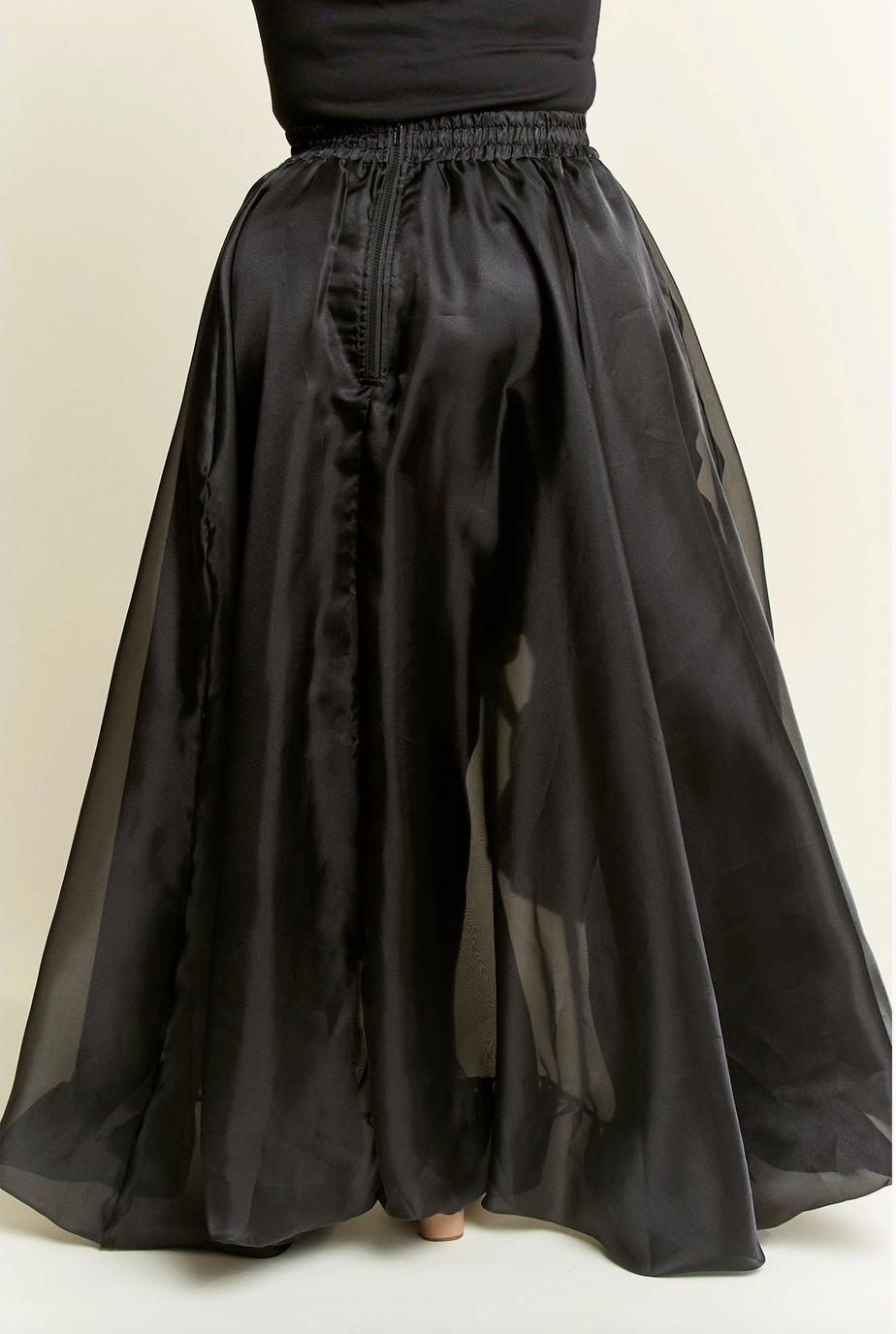 A model wearing a high-low plus sized black skirt with dramatic ruffles, featuring a tie waist and cascading layers.