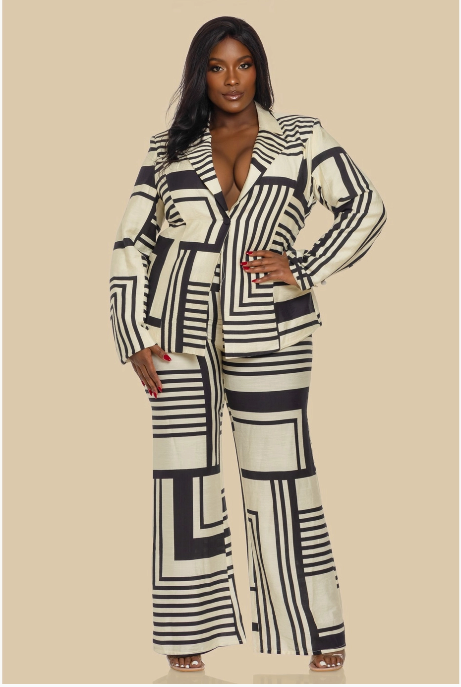 A plus sized woman modeling a black and cream geometric patterned pantsuit with a tailored blazer and bootcut slacks.