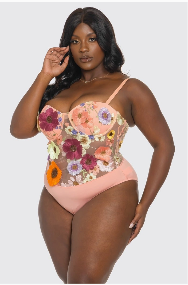 A woman wearing a pink floral bodysuit with 3-D flowers and adjustable straps.
