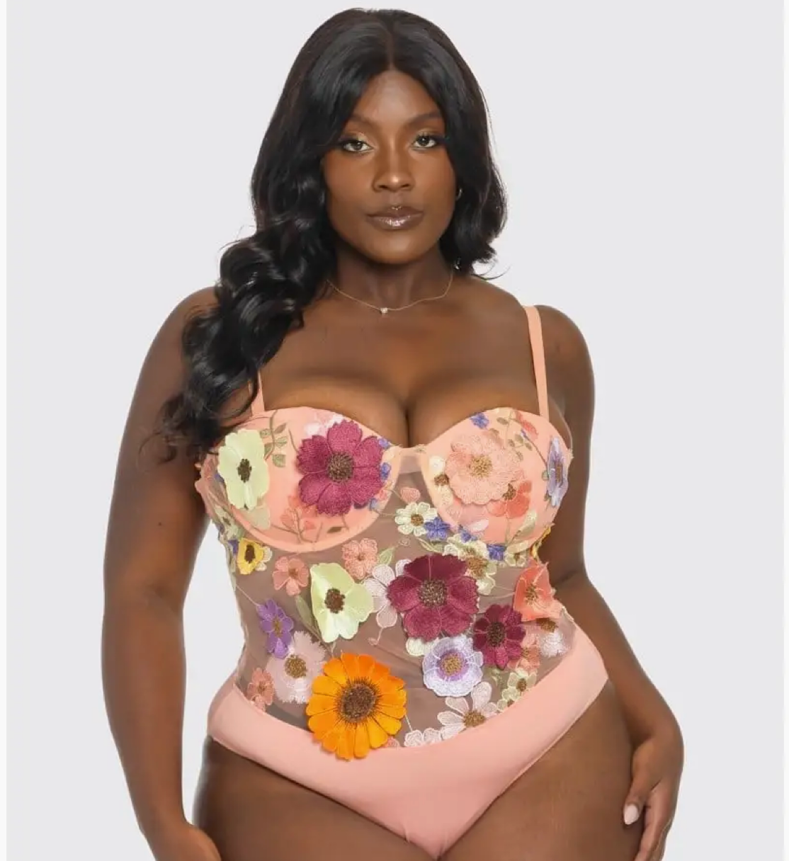 A woman wearing a pink floral bodysuit with 3-D flowers and adjustable straps.