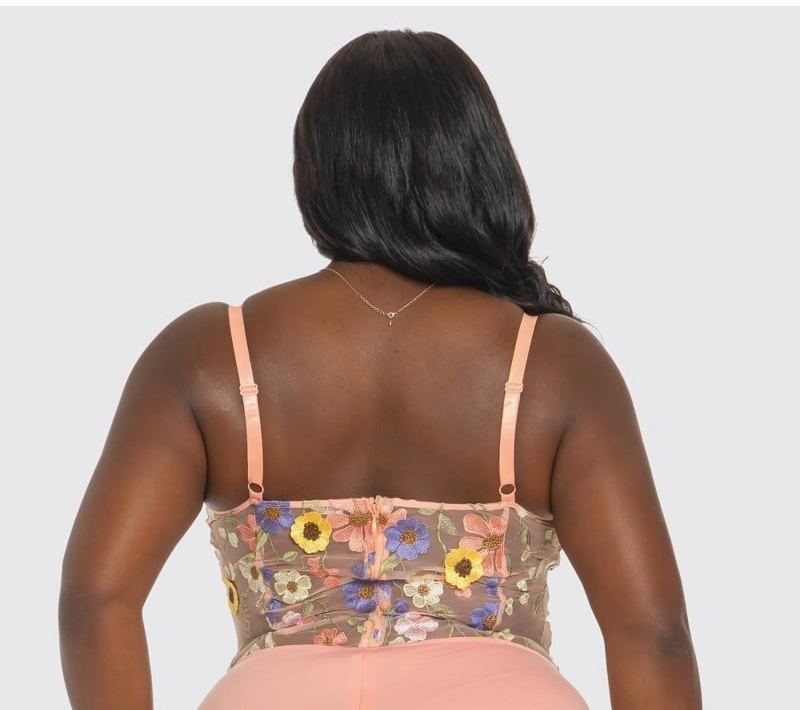 The back of a woman wearing a pink floral bodysuit with 3-D flowers and adjustable straps.