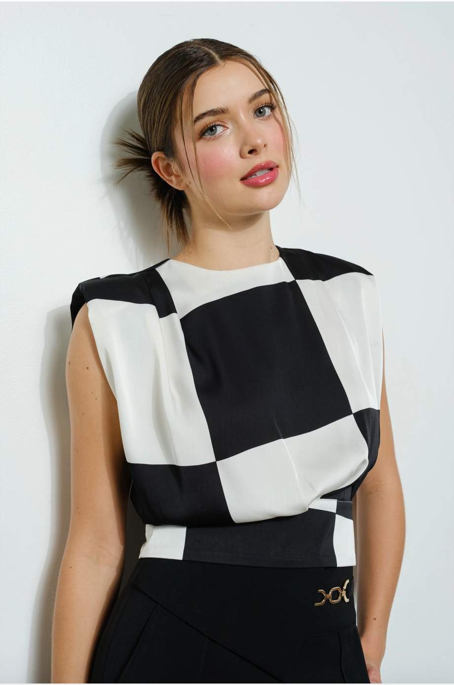 A woman wearing a sleeveless black and white checkered blouse with structured shoulders.