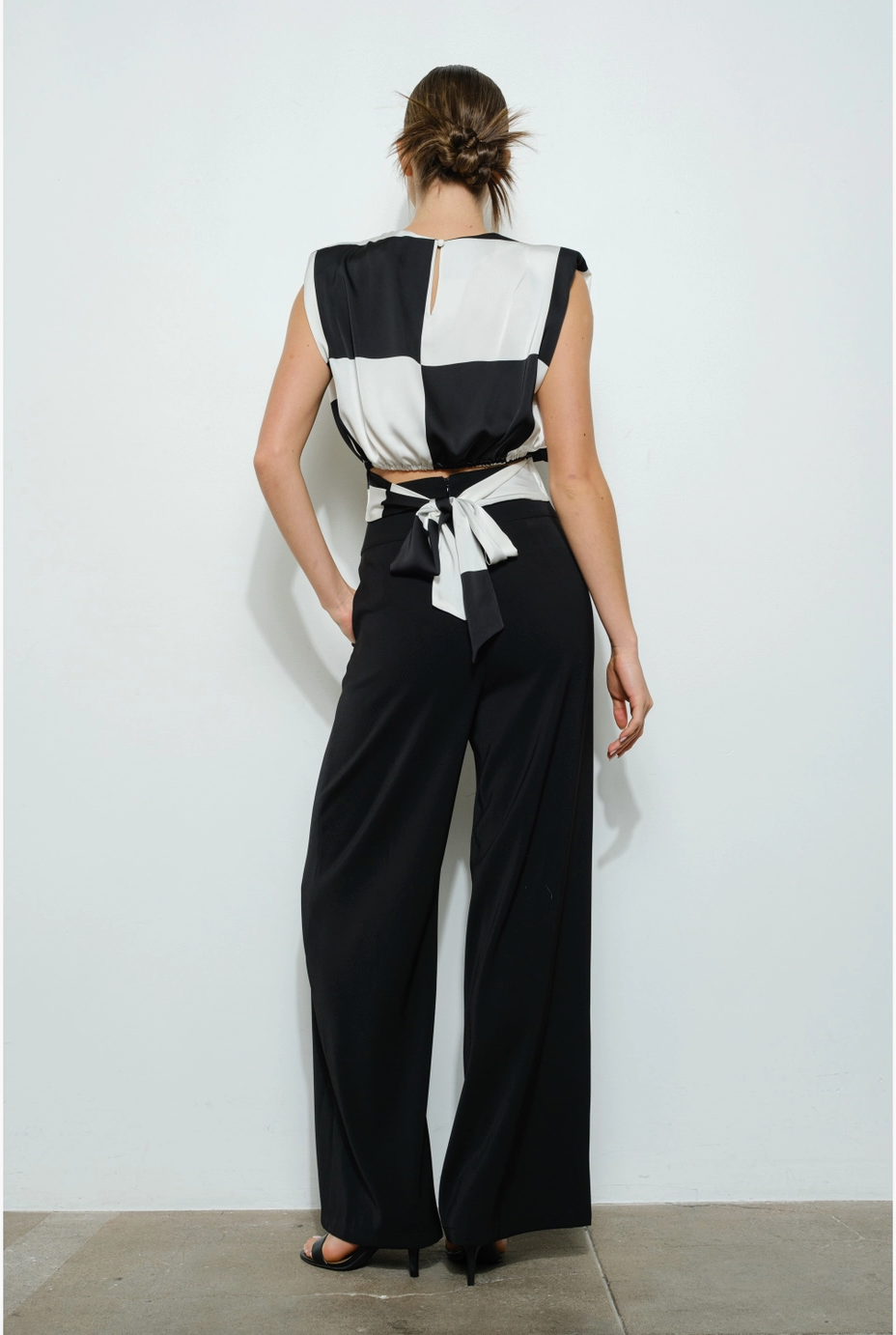 The back of a woman wearing a sleeveless black and white checkered blouse with structured shoulders.