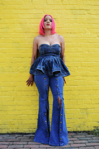 Woman wearing long denim flare jeans that have bronze buttons up the leg. 