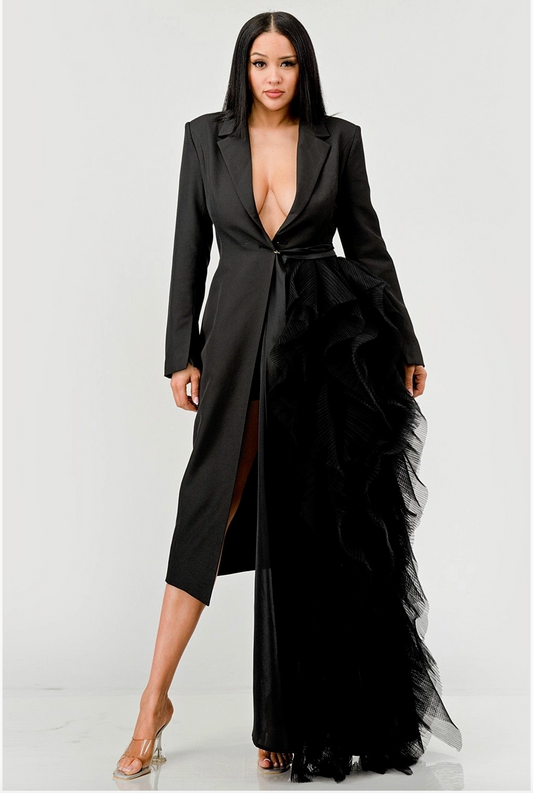 A woman wearing a black tuxedo dress with a plunging neckline and asymmetrical ruffle detail.