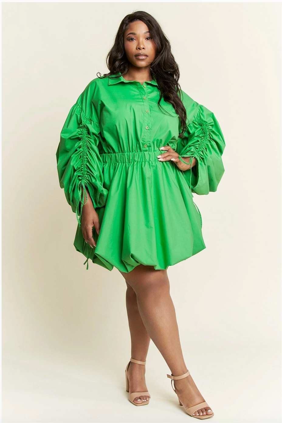 A woman wearing a plus-sized green dress with voluminous ruched sleeves and a cinched waist, paired with heels.