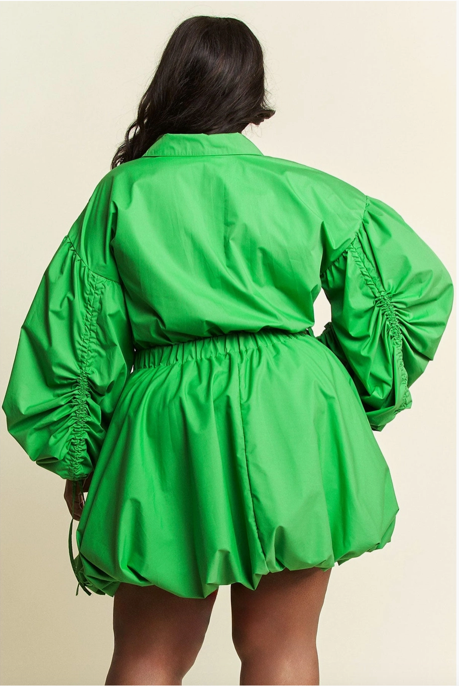 The back of a woman wearing a plus-sized green dress with voluminous ruched sleeves and a cinched waist, paired with heels.