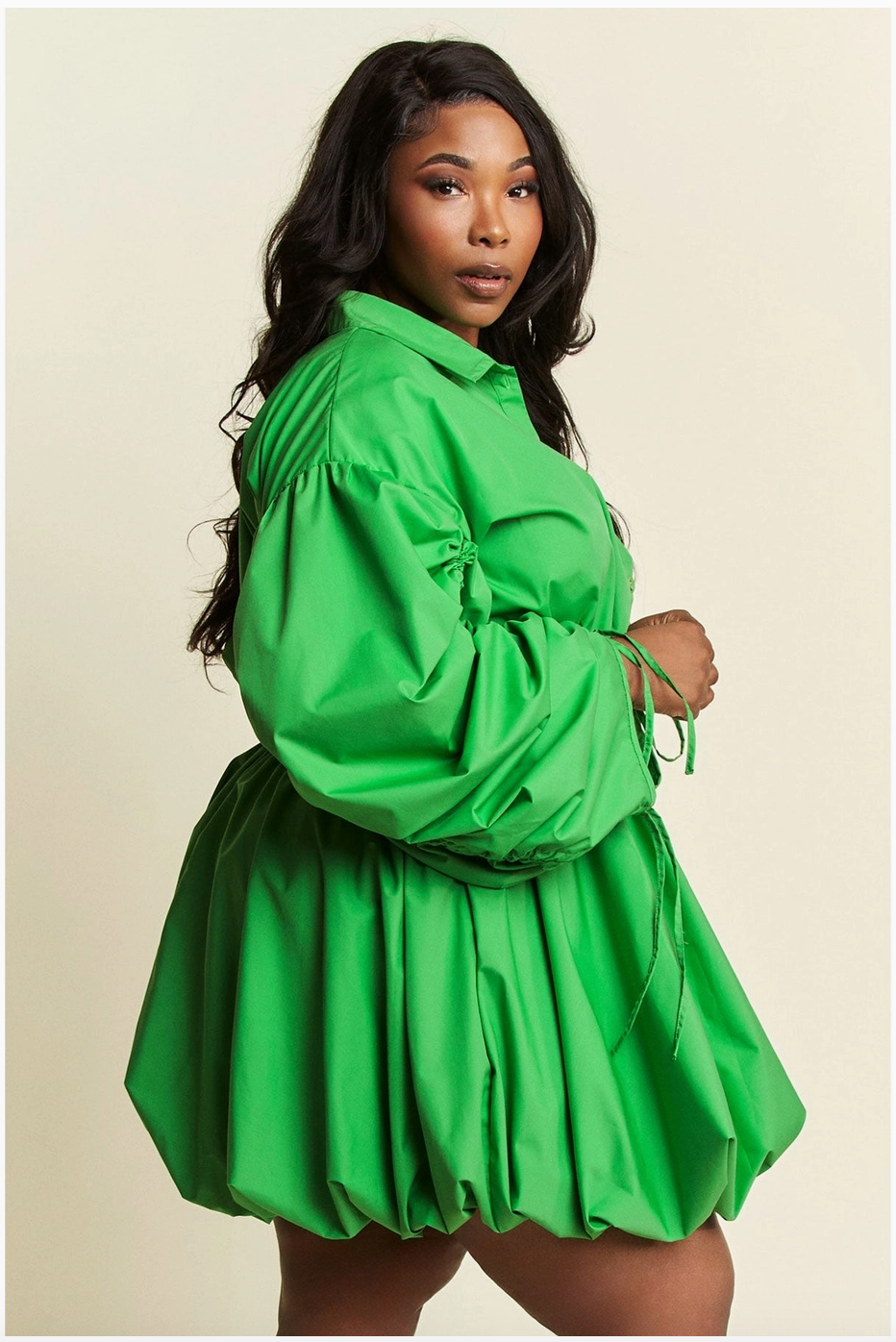 The side view of a woman wearing a plus-sized green dress with voluminous ruched sleeves and a cinched waist, paired with heels.
