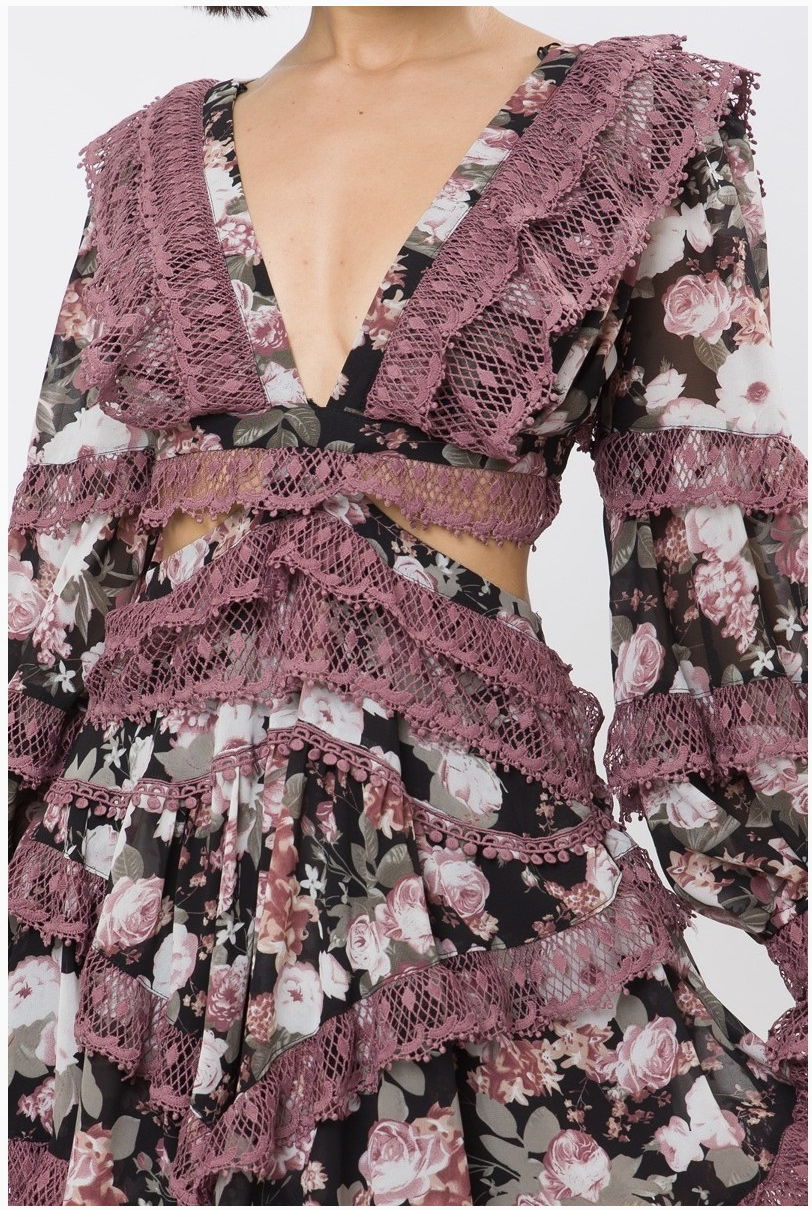 An up close look at the details of a floral lace dress with long sleeves and a plunging neckline, featuring intricate lace detailing and tiered ruffles.