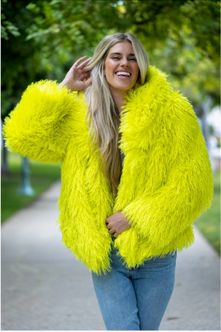 A woman wearing a waist length bright yellow faux fur coat.