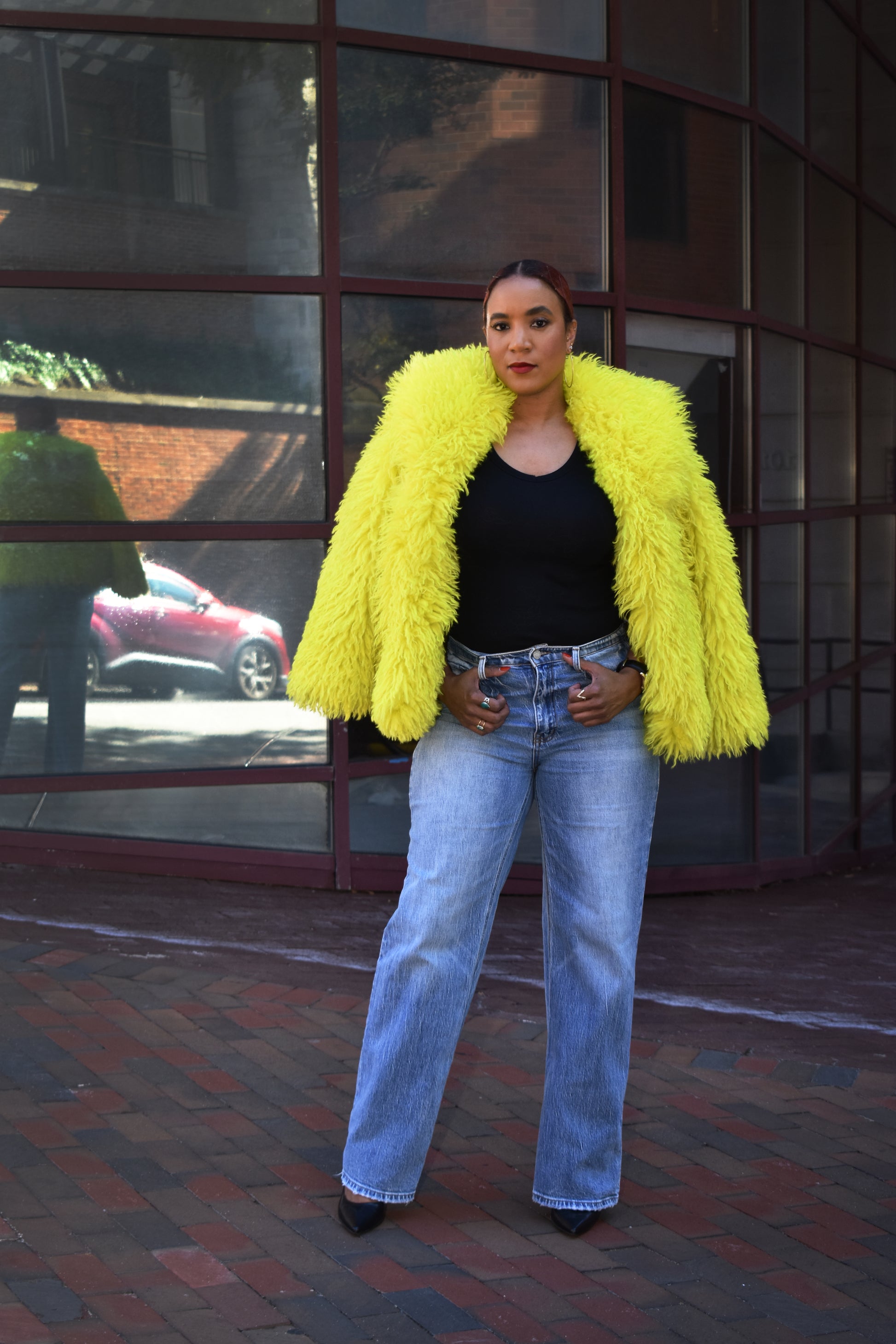 Woman wearing a bright yellow faux fur jacket with straight leg blue jeans.