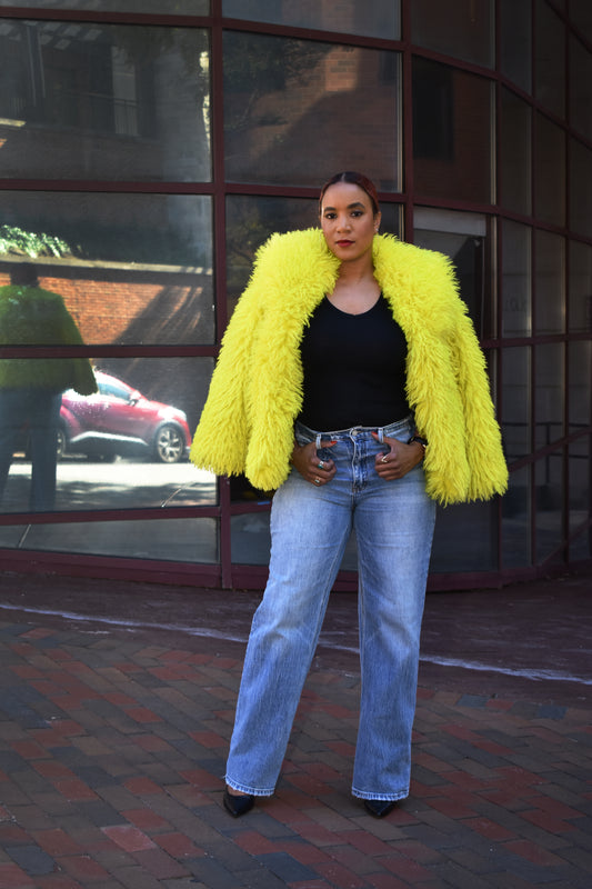 Woman wearing a bright yellow faux fur jacket with straight leg blue jeans.