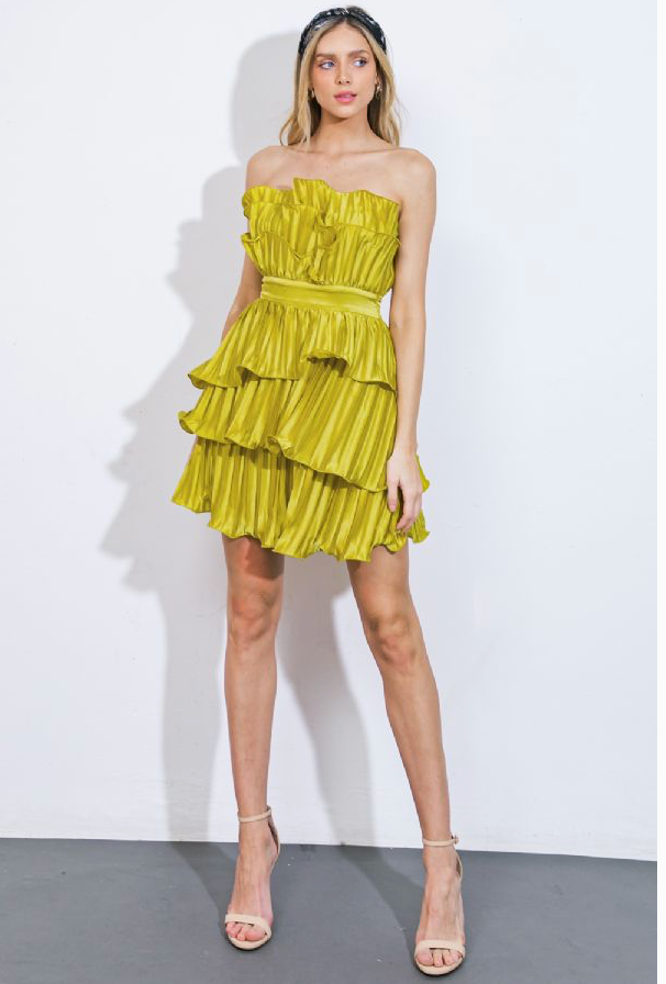 Woman wearing a strapless, short, vibrant green dress. The dress features cascading ruffles, a fitted waistband, and a pleated fabric design.