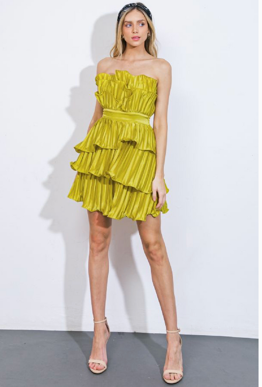 Woman wearing a strapless, short, vibrant green dress. The dress features cascading ruffles, a fitted waistband, and a pleated fabric design.