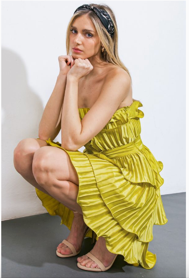 Woman wearing a strapless, short, vibrant green dress. The dress features cascading ruffles, a fitted waistband, and a pleated fabric design.