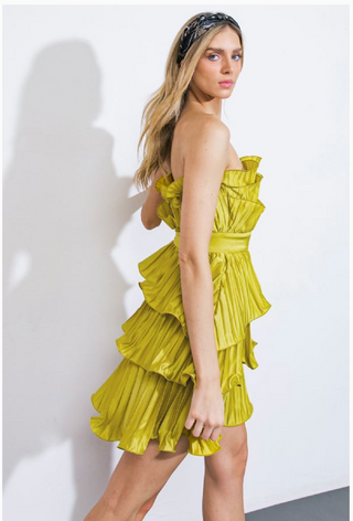 Woman wearing a strapless, short, vibrant green dress. The dress features cascading ruffles, a fitted waistband, and a pleated fabric design.