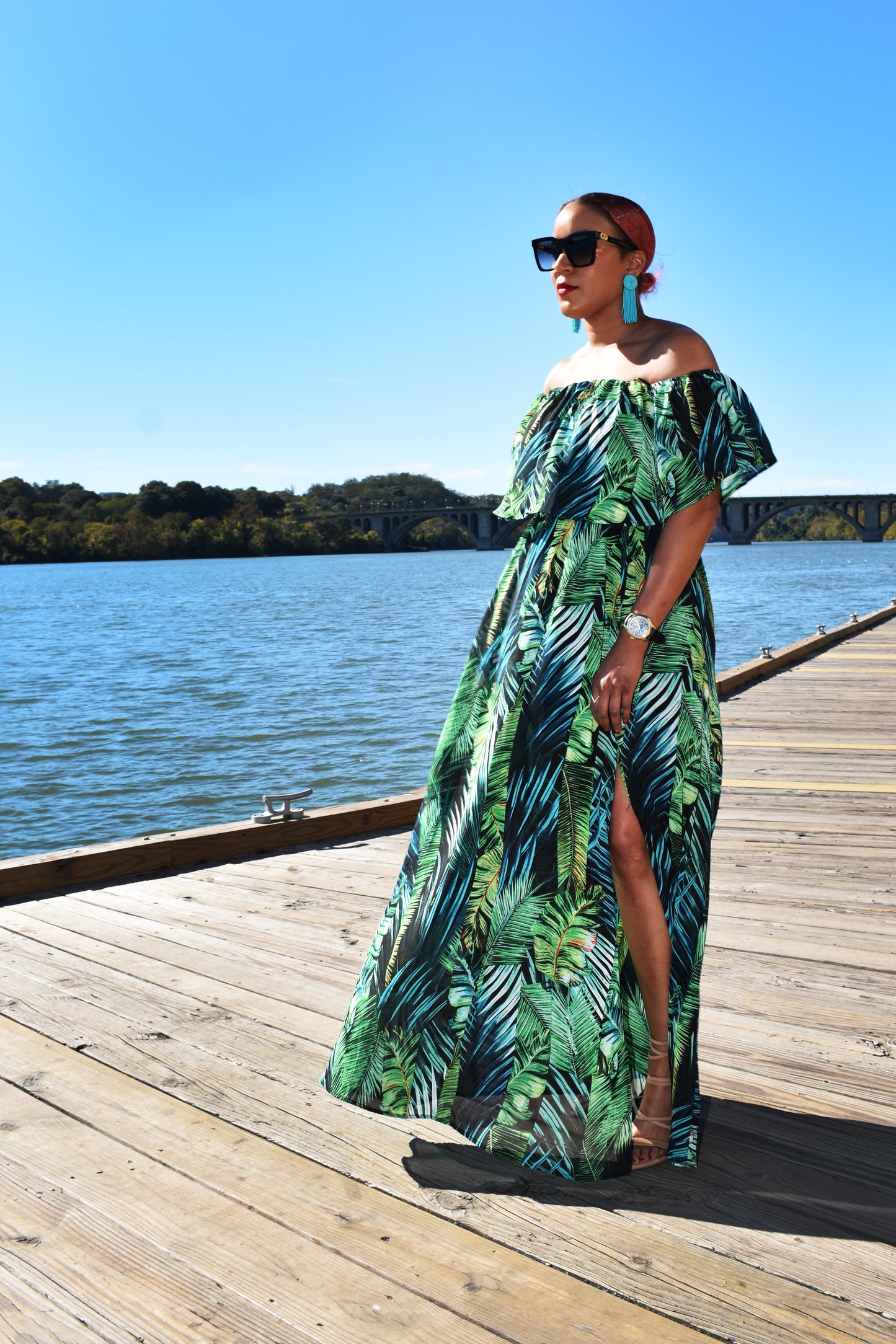 Woman wearing the Island Breeze Maxi Dress, a green tropical dress with palm leaves all across it. 