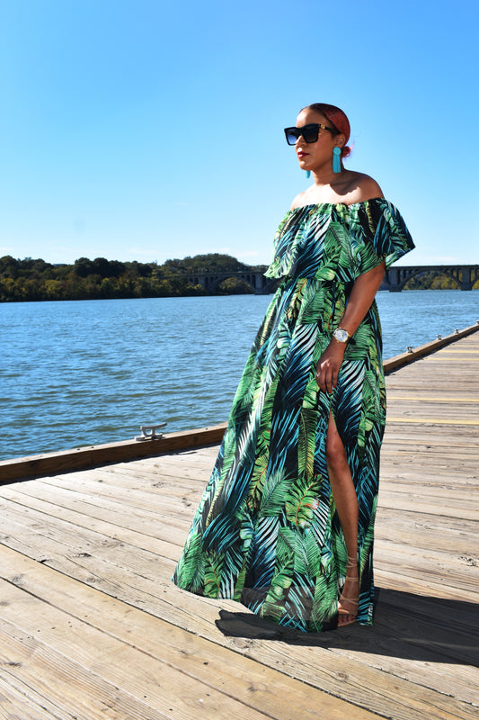 Woman wearing the Island Breeze Maxi Dress, a green tropical dress with palm leaves all across it. 