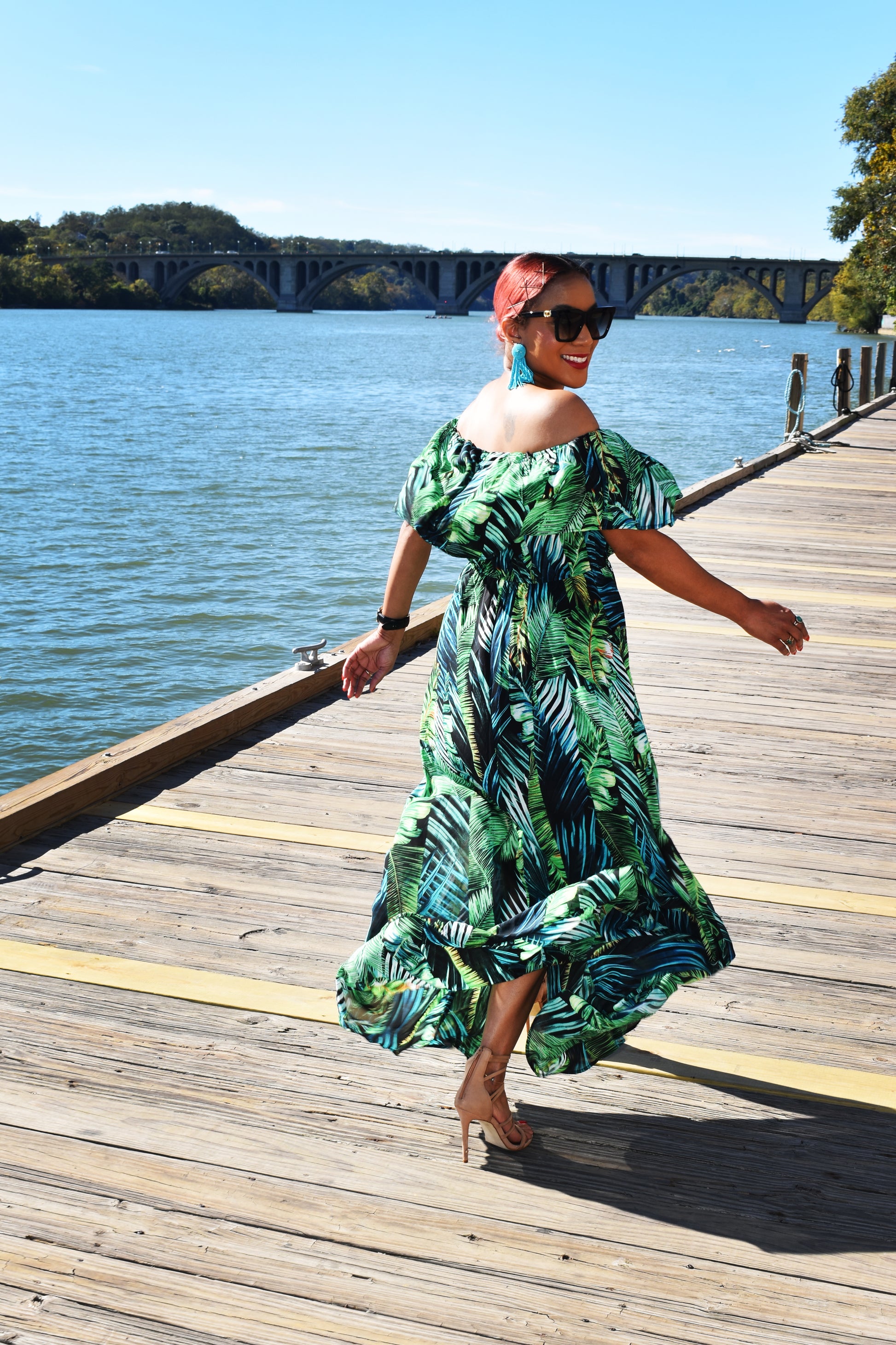 Woman looking over her shoulder as she walks away wearing the Island Breeze Maxi Dress, a green tropical dress with palm leaves all across it. 