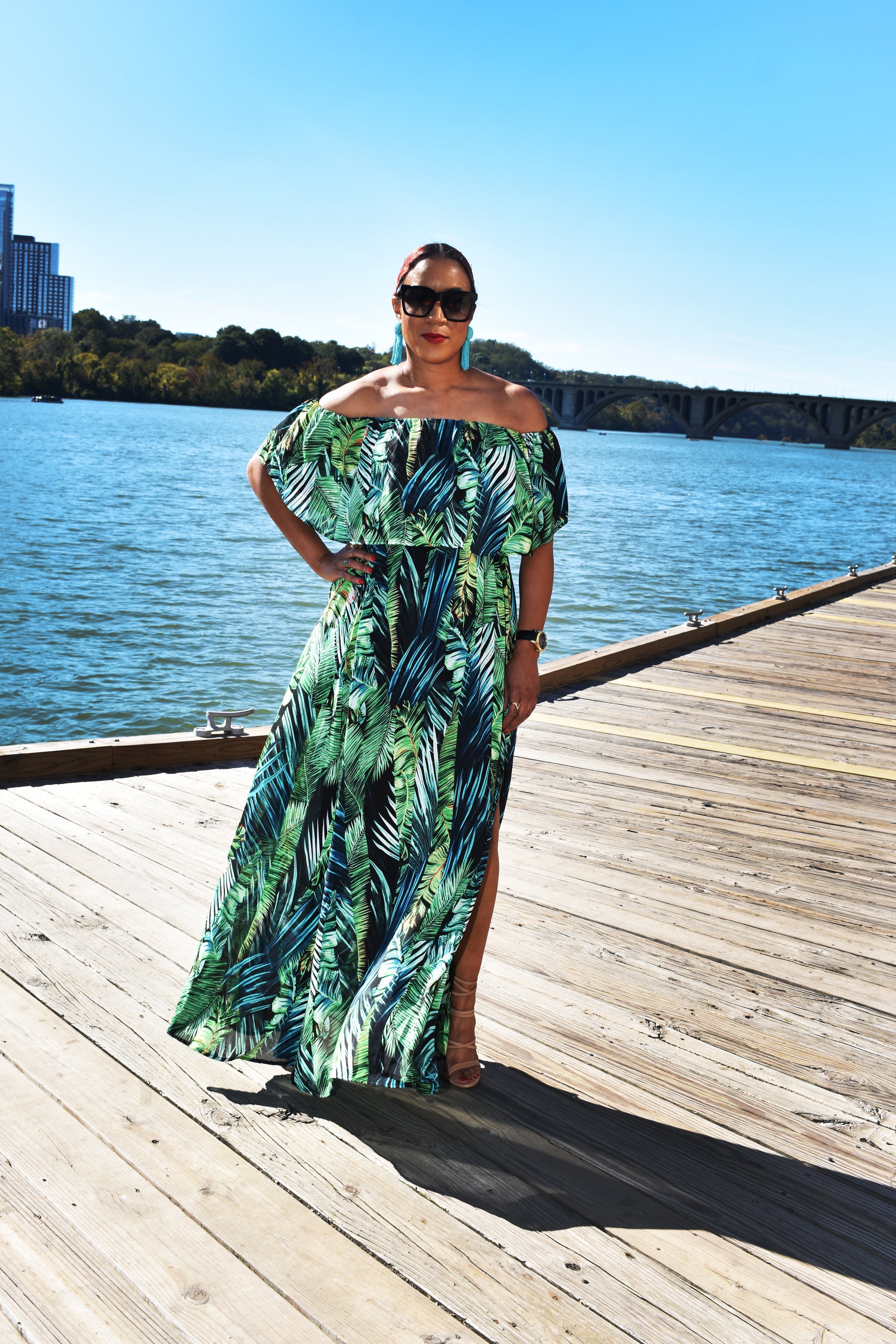 Woman wearing the Island Breeze Maxi Dress, a green tropical dress with palm leaves all across it. 