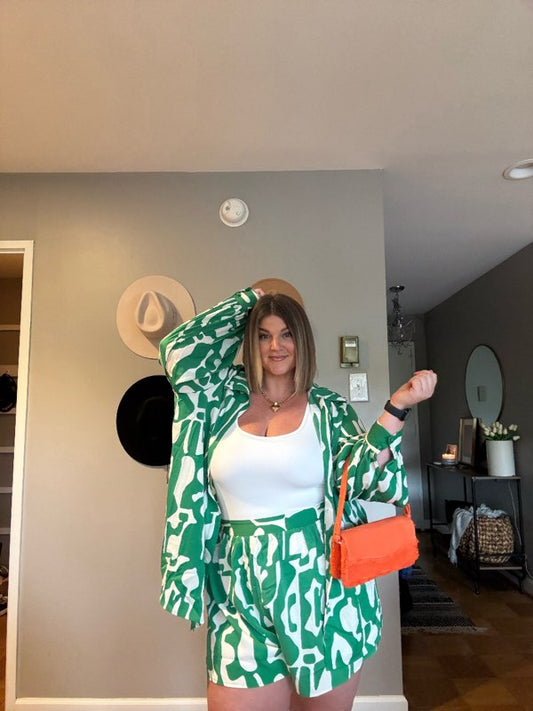 A woman wearing a green and white plus-sized shorts set with long sleeves and a collared neckline, paired with white tank top and an orange handbag.