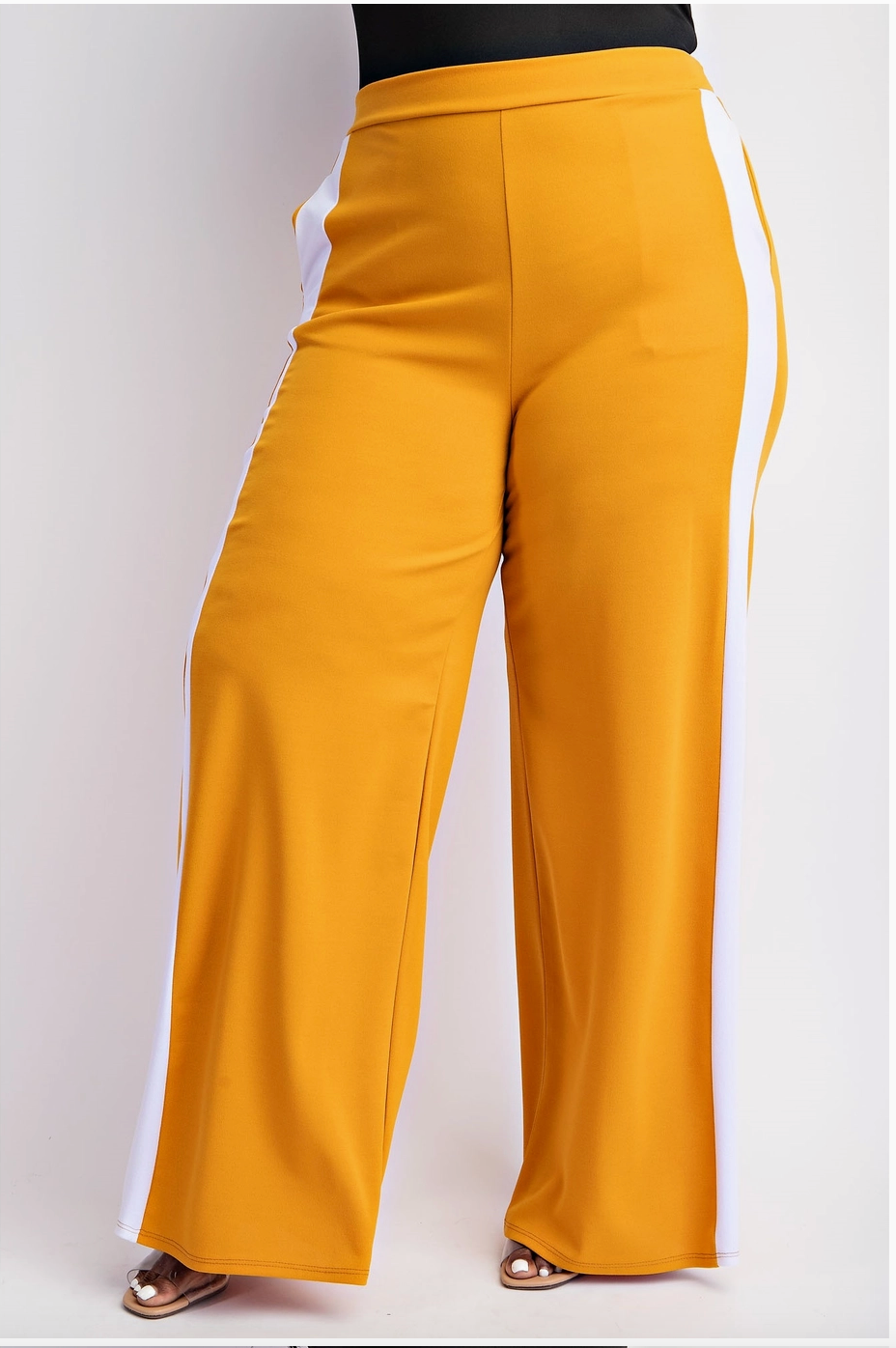 A woman wearing mustard yellow plus sized track pants with sporty side stripes and an elastic waistband.