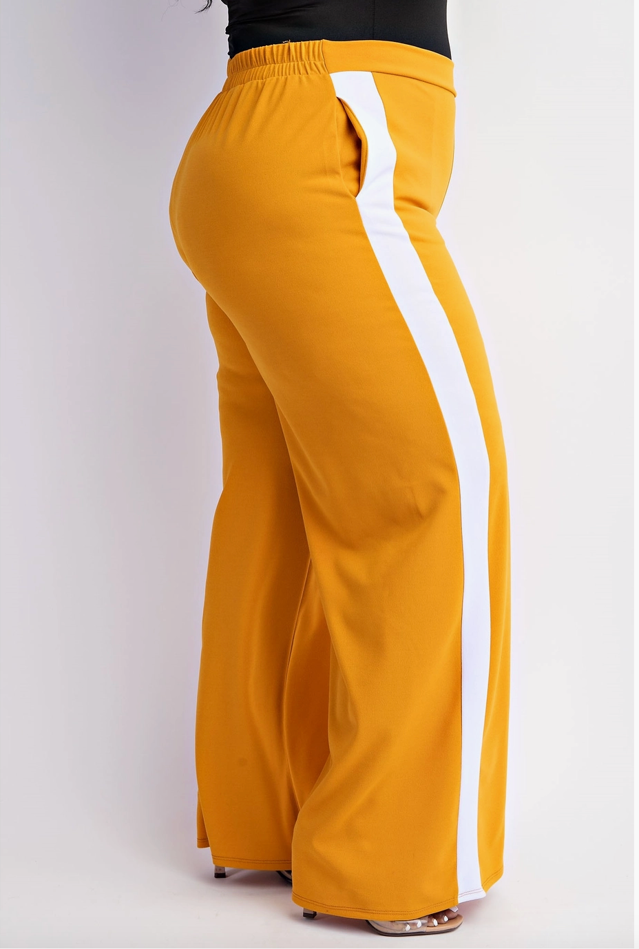 The side view of a woman wearing mustard yellow plus sized track pants with sporty side stripes and an elastic waistband.