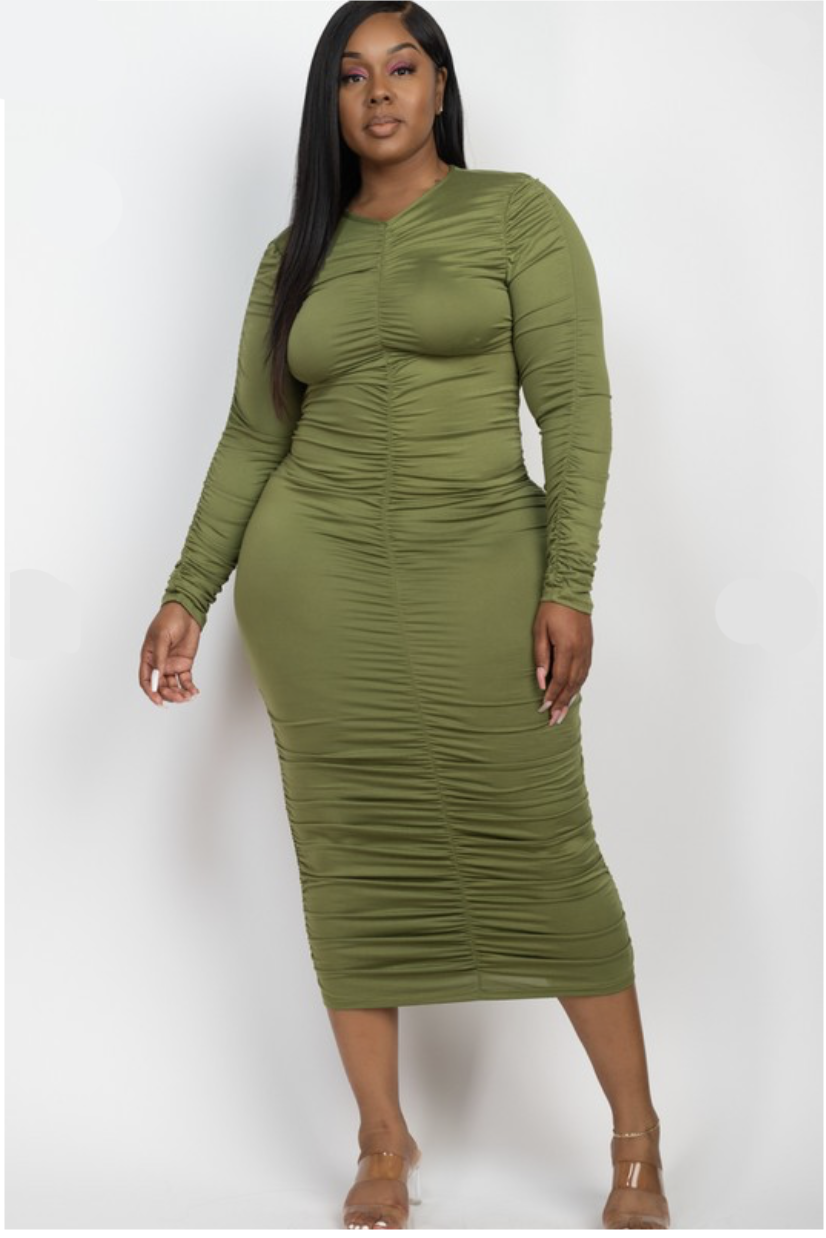 A woman wearing an olive green long-sleeved ruched plus sized dress that reaches midi length.
