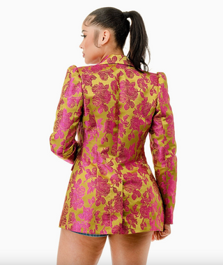 Woman wearing the Opulent Bloom Blazer, a luxurious floral brocade blazer in fuchsia and lime green. The blazer features a structured silhouette, notched lapel, and single-breasted button closure, creating a chic and sophisticated look.