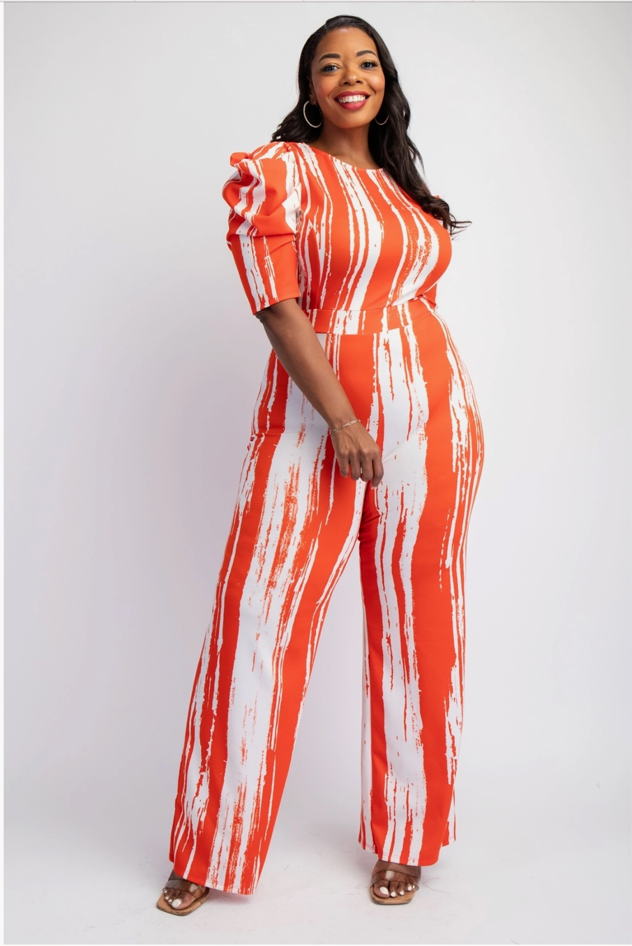 A woman wearing a vibrant orange and white striped plus-sized jumpsuit with a tailored fit and puff sleeves.