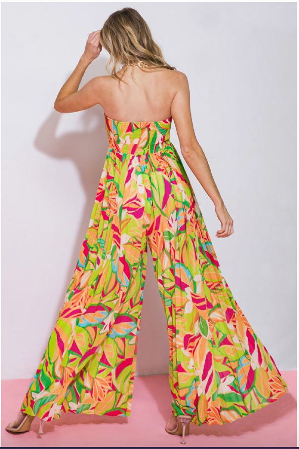 The back of a woman wearing a multicolored jumpsuit with a sweetheart neckline and long, flowy, pleated pants with her leg kicked out.