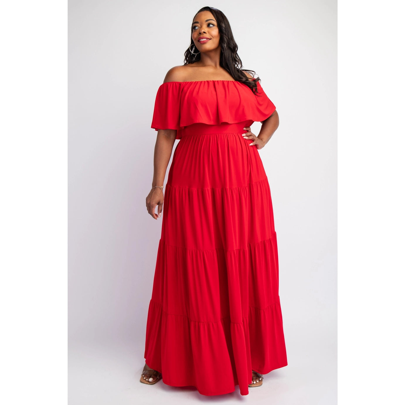 A plus sized woman wearing a red, off-the-shoulder, maxi dress with ruffled sleeves and a tiered skirt.