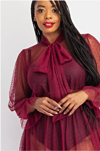 Plus sized woman wearing a sheer blouse with a bow in burgundy.