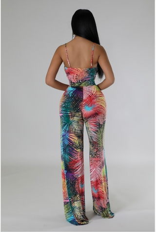 A woman wearing a vibrant, multicolor tropical print jumpsuit with a form-fitting bodice and wide-leg pants.