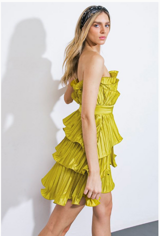 Woman wearing a strapless, short, vibrant green dress called Green Tulip Dress. The dress features cascading ruffles, a fitted waistband, and a pleated fabric design.