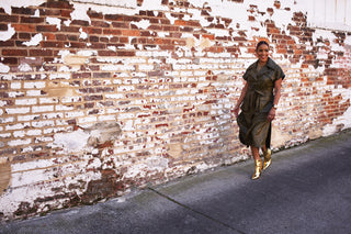 A woman wearing a green vegan leather jacket with short sleeves and oversized lapels as a dress. Paired with gold booties.