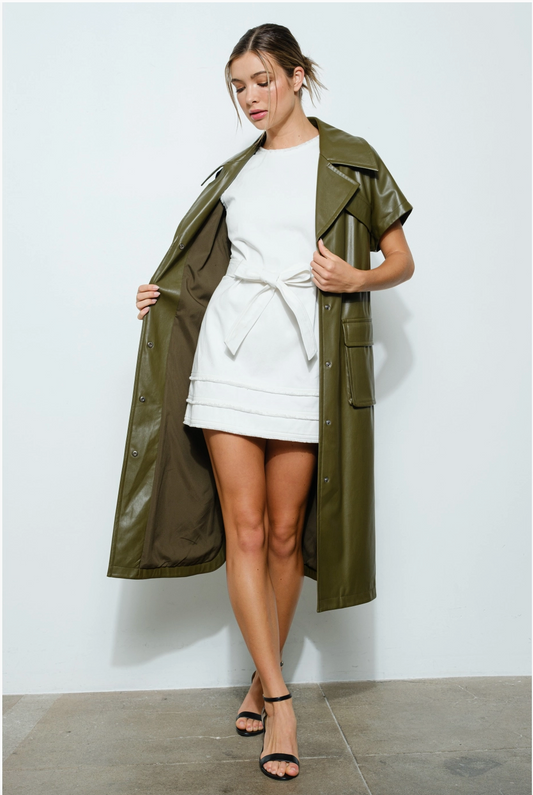 A woman wearing a green vegan leather jacket with short sleeves and oversized lapels, paired with a white dress.