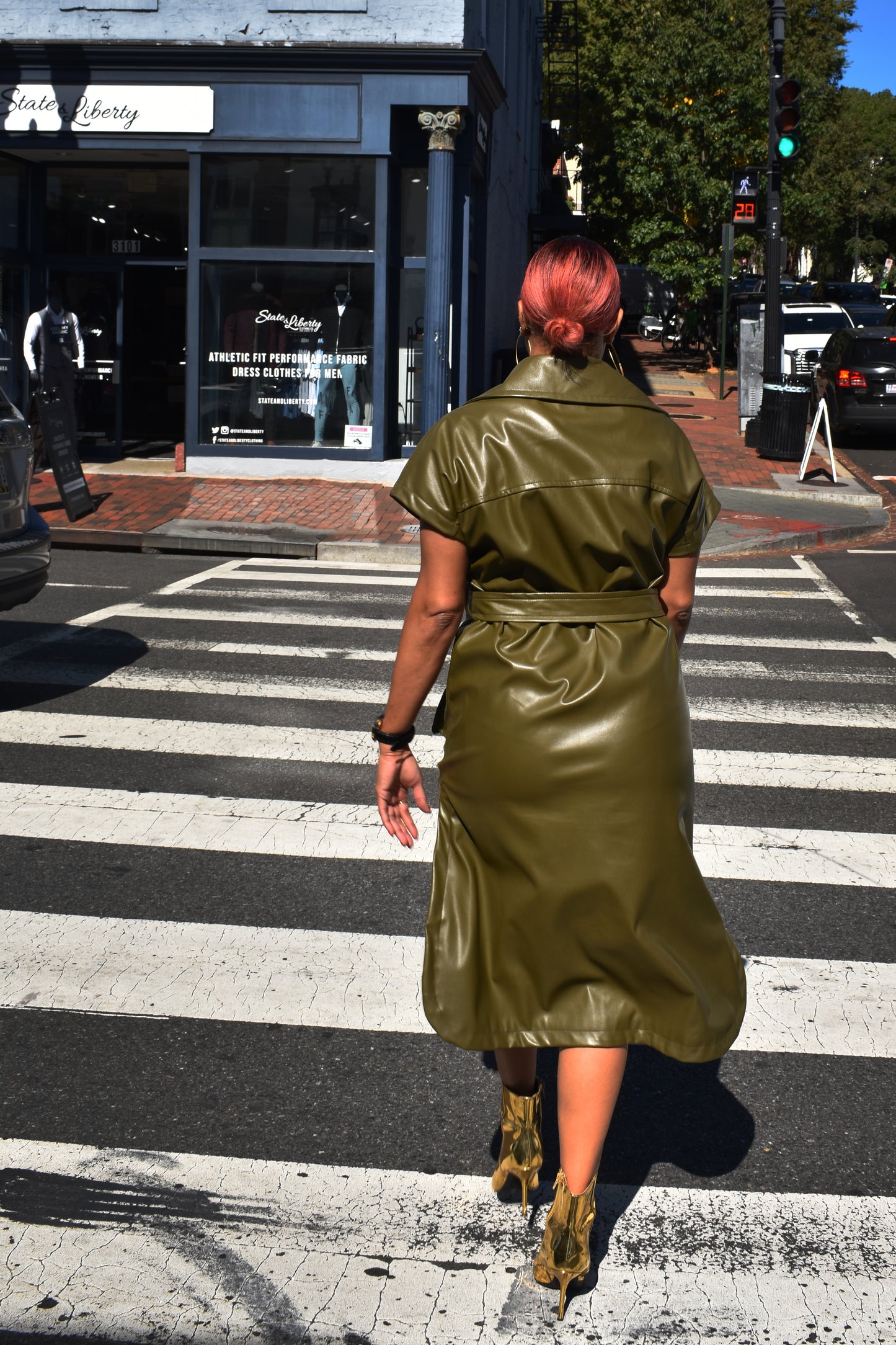 A woman wearing a green vegan leather jacket with short sleeves and oversized lapels, walking across a busy city street.
