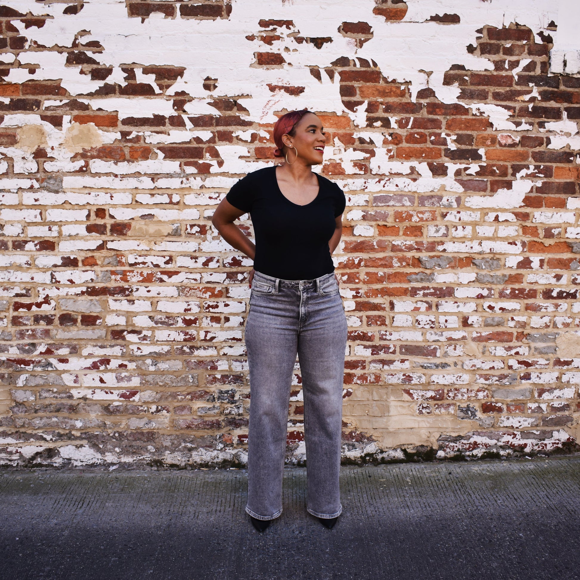 Woman wearing The Olivia - Grey Wide Leg Jeans in front of a brick wall.