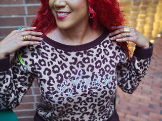 Woman wearing a leopard print sweater with the name e.Laniese embroidered across the chess. 